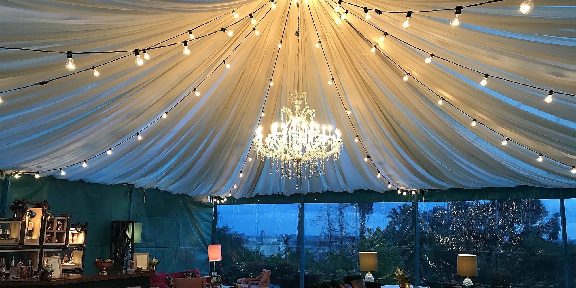 Draped tent ceiling with a crystal chandelier and string lights at an Absolut Elyx event