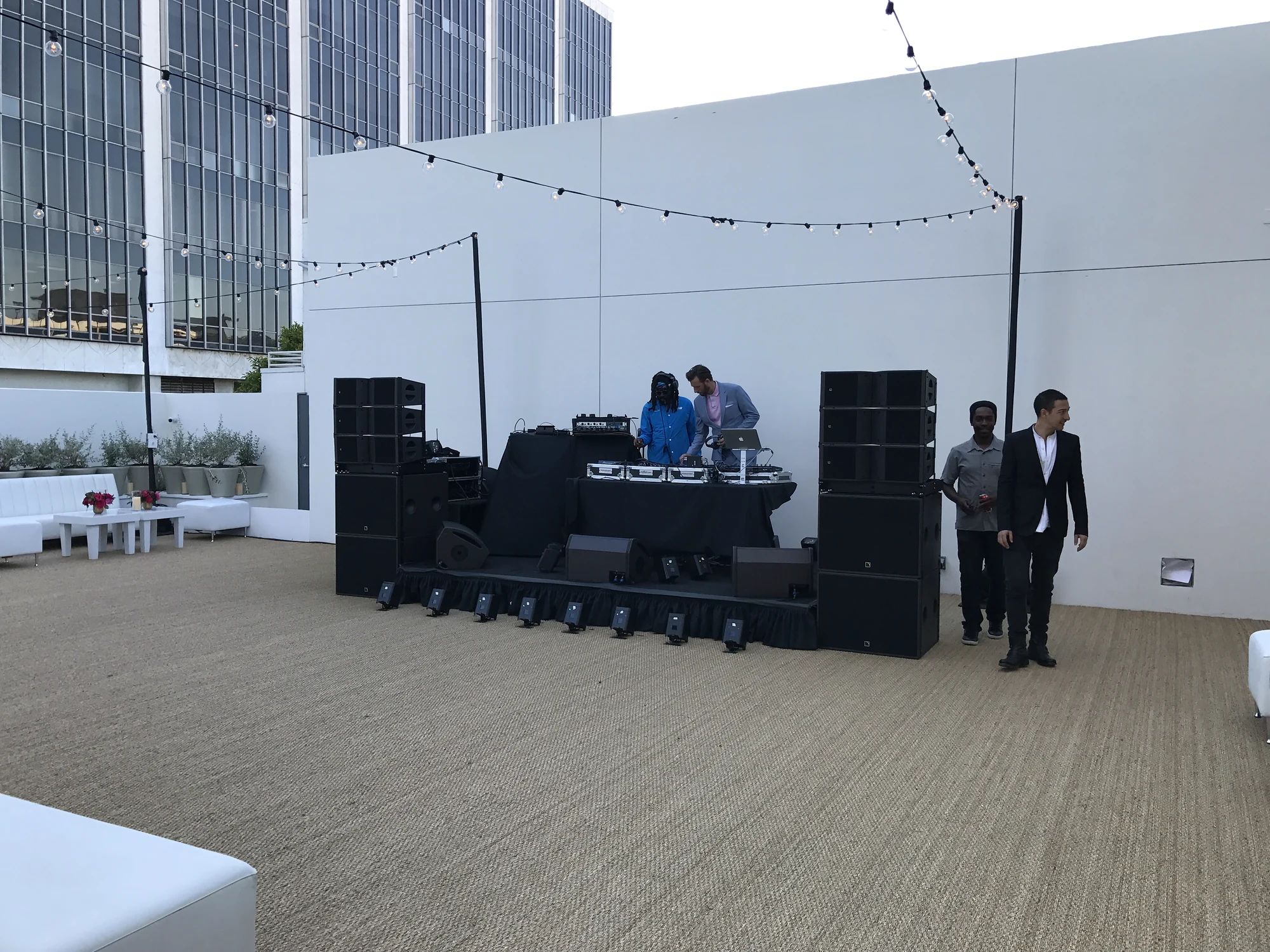 AVE rooftop production at Christie's: a DJ booth flanked by speaker stacks under string lights